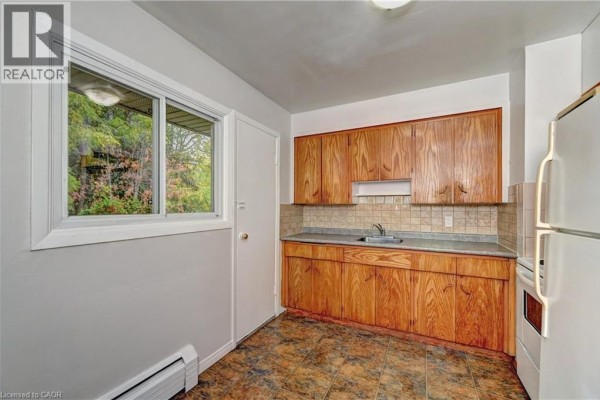 Kitchen area with light wood cabinets, beige tiled backsplash, and a window overlooking greenery. - 280 Sydney Street S Unit# A6, Kitchener