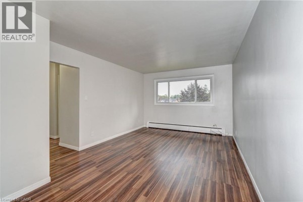 Living room with dark wood laminate flooring, white walls, and a large window with a view. - 280 Sydney Street S Unit# A6, Kitchener