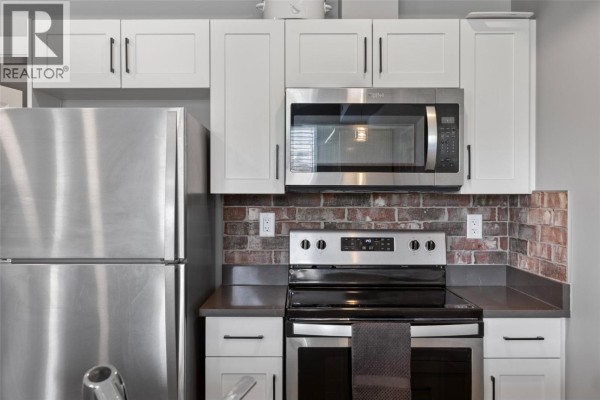 Open-concept living and kitchen area with a balcony door, white doors, and view of laundry appliances. - 280 Tranquille Road Unit# 312, Kamloops