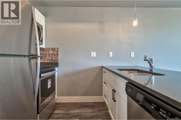 Kitchen view showing a stainless steel refrigerator, dishwasher, white cabinets, and a grey island countertop. - 280 Tranquille Road Unit# 312, Kamloops