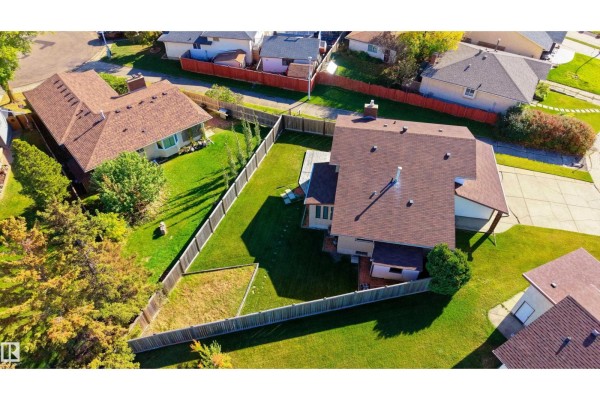 Aerial view of a large, fenced backyard with a green lawn, mature trees, and a wooden deck attached to the house. - 280 Warwick Rd Nw, Edmonton