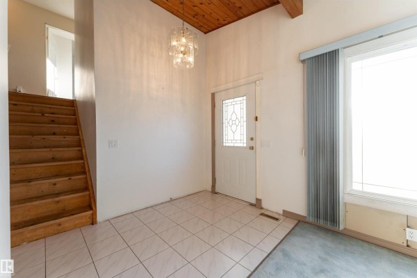 Interior entryway with tiled floor, wooden staircase, white door with decorative glass, and a chandelier. - 280 Warwick Rd Nw, Edmonton