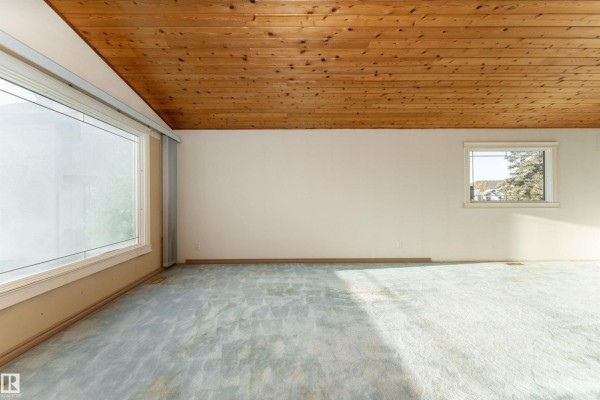 Living room featuring a wood-plank ceiling, large window with blinds, and light blue carpet. - 280 Warwick Rd Nw, Edmonton