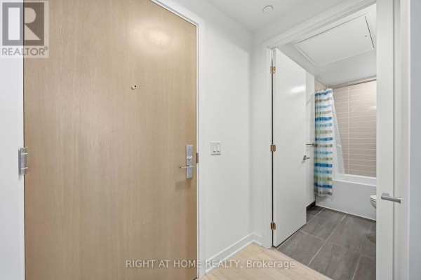 Interior view of an apartment entrance door and an open bathroom door with a bathtub and shower curtain. - 2801 - 357 King Street W, Toronto