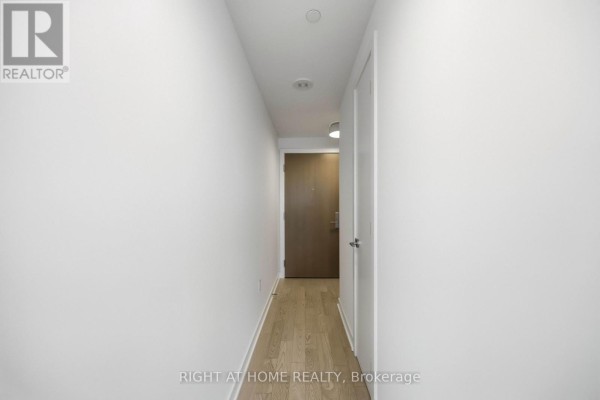 Interior hallway of a modern apartment with white walls, light wood floors, and a closed door ahead. - 2801 - 357 King Street W, Toronto