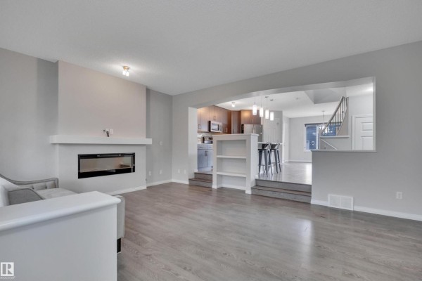 Living room with a modern fireplace and view into the kitchen and dining area. - 2801 Coughlan Green Gr Sw, Edmonton