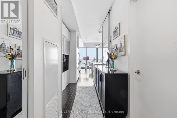 Hallway with dark wood floors, black credenzas, and artwork, leading towards a bright living area and window view. - 2805 - 390 Cherry Street, Toronto