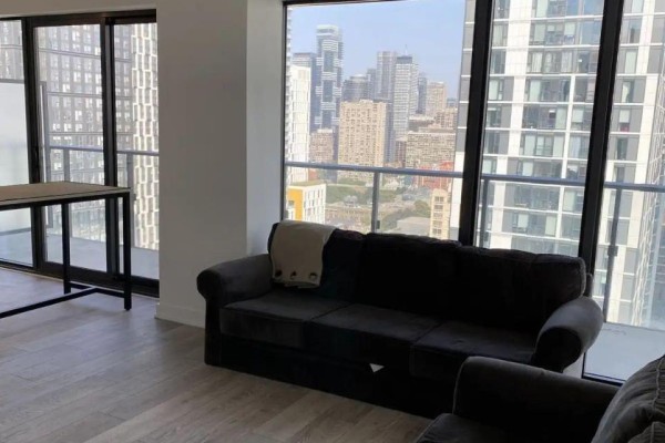 Living area with a dark sofa, light wood floors, and a large window with city views. - 2805 - 47 Mutual Street, Toronto