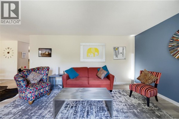 Living room with a red sofa, patterned chairs, metal coffee table, and artwork on the walls. - 2806 35 Street Unit# 207, Vernon