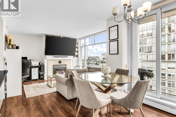 Living and dining area with a fireplace, large television, glass dining table, and chairs. - 2807 1199 Marinaside Crescent, Vancouver