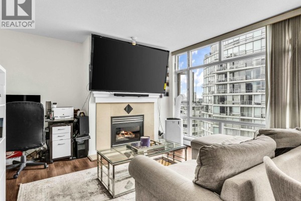 Living room showcasing a fireplace, mounted television, desk area, and cityscape view. - 2807 1199 Marinaside Crescent, Vancouver