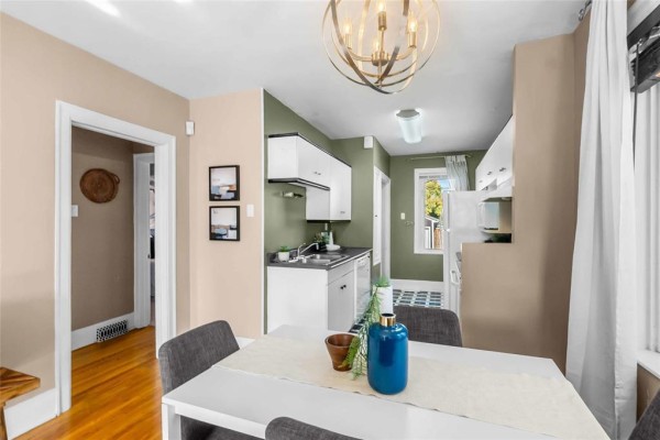 View of the dining table and kitchen area with white cabinets and green accent wall. - 281 Lansdowne Avenue, Winnipeg