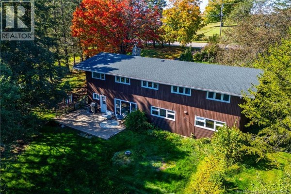Rear view of a two-story brown house with a large deck and wooded backyard on a sunny autumn day. - 281 Main Street, Sackville