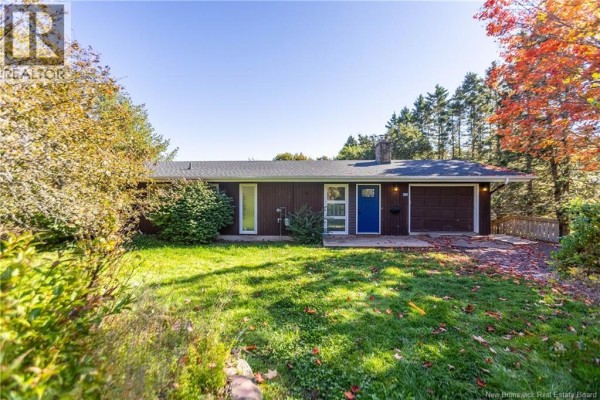 Front view of a single-story brown house with a blue front door and attached garage on a sunny autumn day. - 281 Main Street, Sackville