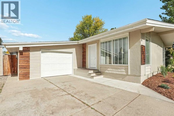Close-up of the beige bungalow exterior showing the garage door, front entrance, and light wood paneling. - 2811 13 Avenue S, Lethbridge