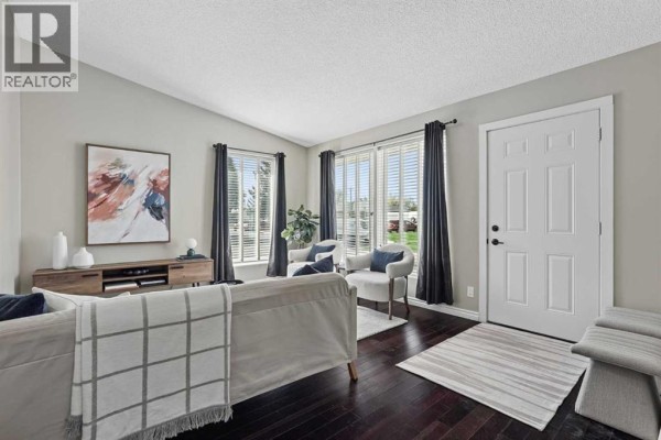 Living room with a fireplace, large windows, dark wood floors, and white and grey furniture. - 2811 13 Avenue S, Lethbridge