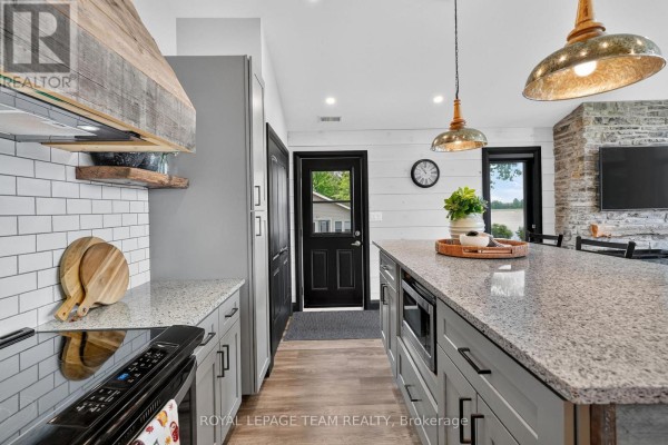 Modern kitchen with granite island, subway tile, and wood beam range hood - 2815 Golf Course Lane North Grenville