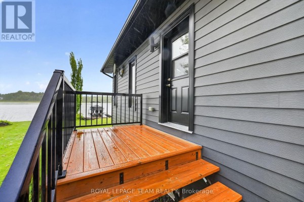 Wet wooden deck & black railing to front door overlooking lake with boat dock - 2815 Golf Course Lane North Grenville