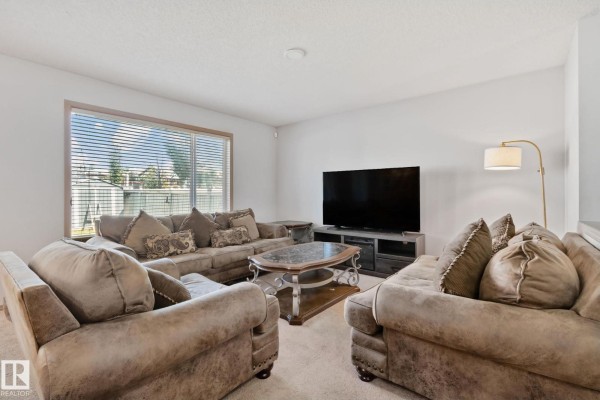Living room with beige sofas, a marble coffee table, and a large television against a white wall. - 2819 33 St Nw Nw, Edmonton