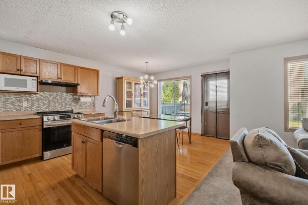 Kitchen with light wood cabinets, stainless steel appliances, and a central island with a sink. - 2819 33 St Nw Nw, Edmonton