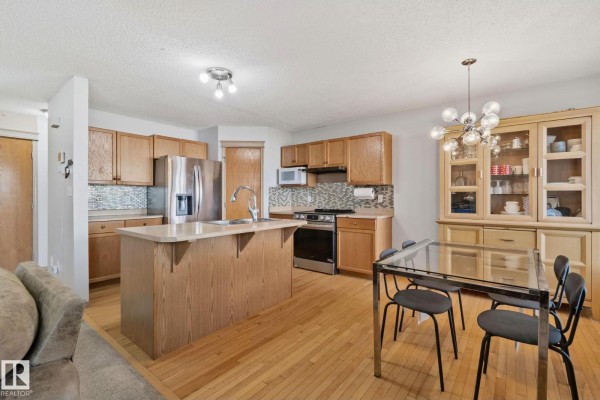 Kitchen and dining area featuring light wood cabinetry, stainless steel appliances, and a glass-top dining table. - 2819 33 St Nw Nw, Edmonton