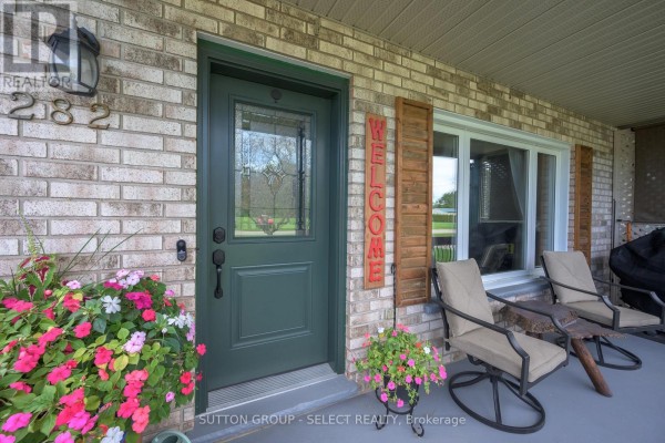 Front door entrance with a green door, window, welcome sign, and chairs on porch. - 282 Marsh Line, Dutton/dunwich