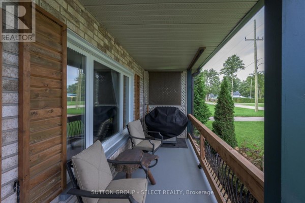Covered front porch with seating, a grill, and views of the street and trees. - 282 Marsh Line, Dutton/dunwich