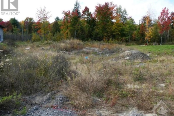 Overgrown vacant lot with dry grass, dirt, and autumn foliage trees. - 282 Roxanne Street, Clarence Rockland