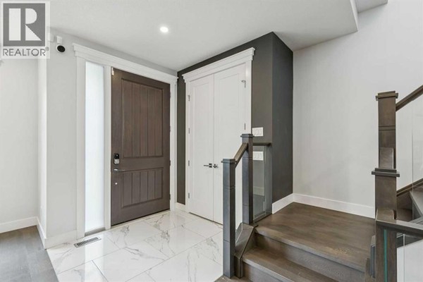 Entrance foyer with a dark wood door, white closet doors, and marble tile floor. - 2826 40 Street Sw, Calgary