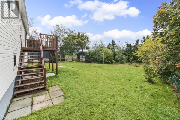 The backyard of the property features a green lawn, wooden stairs leading to a deck, and a small shed. - 283 Fowlers Road, Conception Bay South