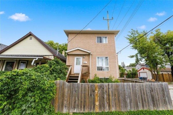 Front view of a two-story house with a stucco exterior and wooden fence. - 283 Mckenzie Street, Winnipeg