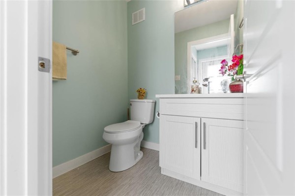 A small powder room with a toilet, white vanity, and light blue walls. - 283 Mckenzie Street, Winnipeg