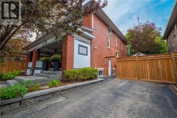 Wicker furniture and a rug on a covered front porch with brick columns and large windows. - 283 Plains Road W, Burlington