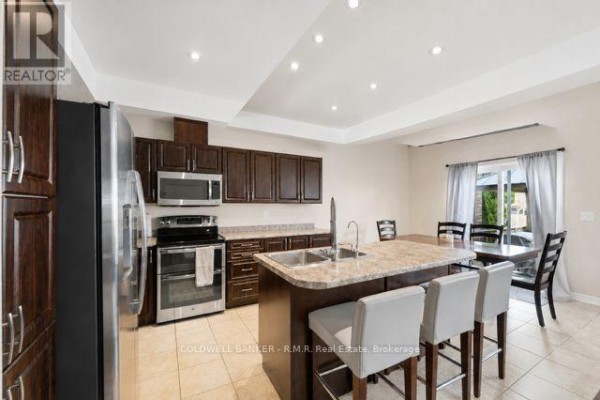Kitchen with dark wood cabinets, granite island with sink, and dining area. - 283 Rollings Street, Cobourg