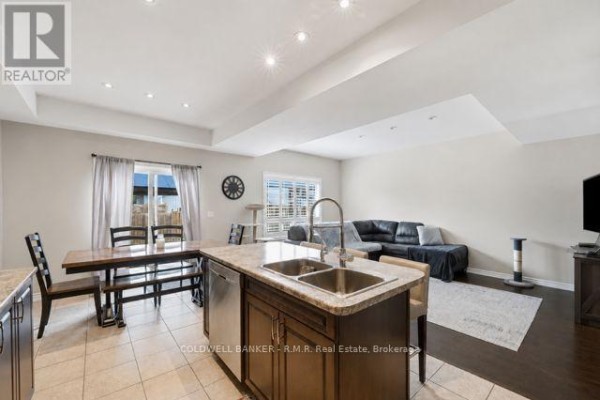 Open concept kitchen, dining, and living area with island and black leather couch. - 283 Rollings Street, Cobourg