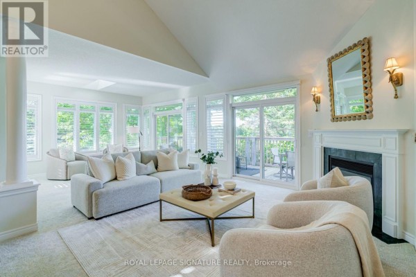 Living room with a fireplace, sofa, chairs, and large windows overlooking a deck and trees. - 285 - 8 Lakeside Vista Way, Markham