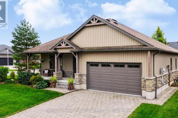 Side view of a beige siding house with a brown garage door, stone accents, and a paved driveway. - 285 Darling Boulevard, South Huron