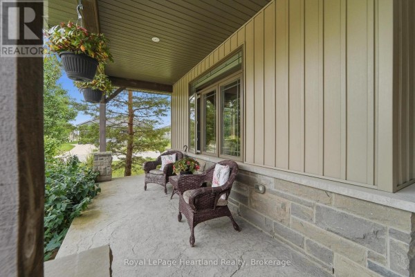 Wicker chairs on a concrete front porch with hanging plants and stone accents. - 285 Darling Boulevard, South Huron