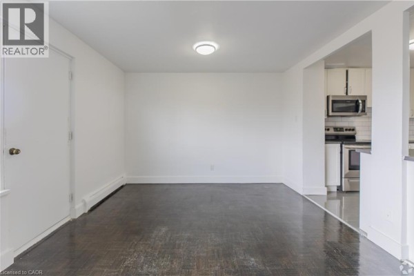 Empty room with dark hardwood floors and white walls, doorway to kitchen. - 285 Erb Street W Unit# 707, Waterloo