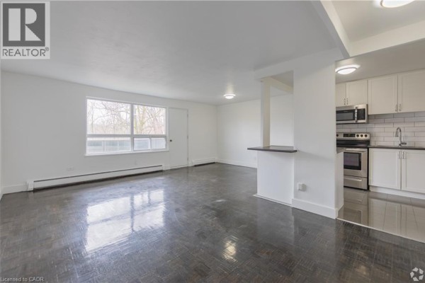 Living area with dark hardwood floors, white walls, and window view. - 285 Erb Street W Unit# 707, Waterloo