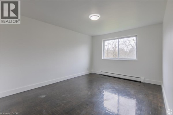 Empty bedroom with dark hardwood floors, white walls, and a window. - 285 Erb Street W Unit# 707, Waterloo