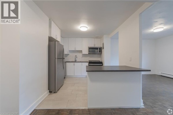 View of the white kitchen with island from the living area. - 285 Erb Street W Unit# 809, Waterloo