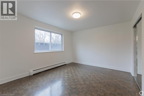 Bedroom with dark wood parquet flooring and large window with mirrored closet. - 285 Erb Street W Unit# 809, Waterloo