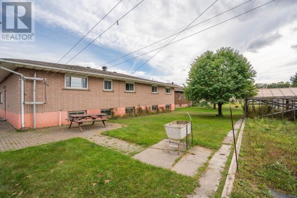 Backyard view with a picnic table, outdoor sink, and a large green lawn. - 285 Spadina Ave, Sault Ste  Marie