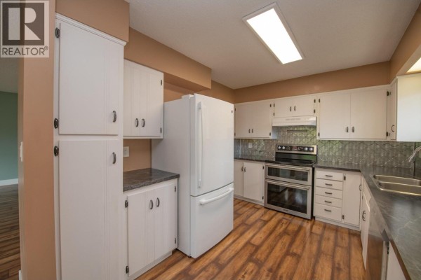 Kitchen with white cabinets, dark countertops, stainless steel appliances, and wood floors, viewed from the side. - 2855 Burns Avenue, Armstrong