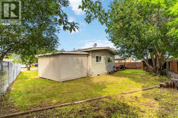 Side and back exterior of the house with beige siding and a view of the green backyard. - 286 Kennedy Bay, Fort Mcmurray