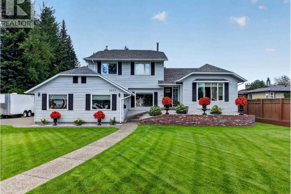 Side view of the house showing the garage door, asphalt driveway, and manicured lawn. - 2869 Ridgeview Drive, Prince George