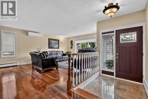 Living room interior featuring a dark leather sofa, hardwood floors, and a front entry door. - 2869 Ridgeview Drive, Prince George