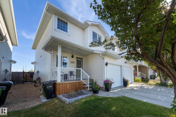 Side exterior view of the beige duplex with a porch and a two-car garage. - 2879 23 St Nw, Edmonton