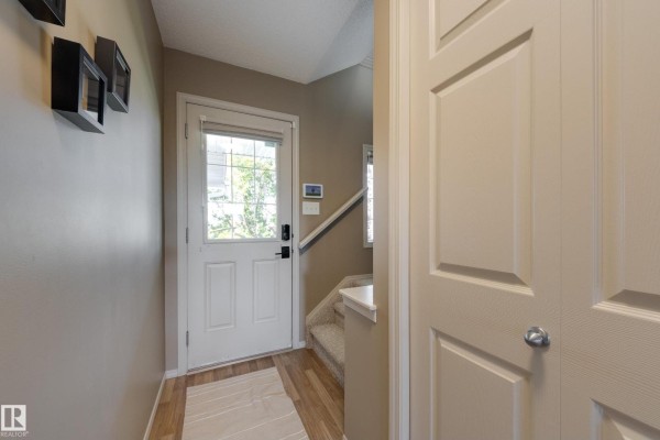 Interior entryway with a white door, glass window, and beige carpeted stairs. - 2879 23 St Nw, Edmonton